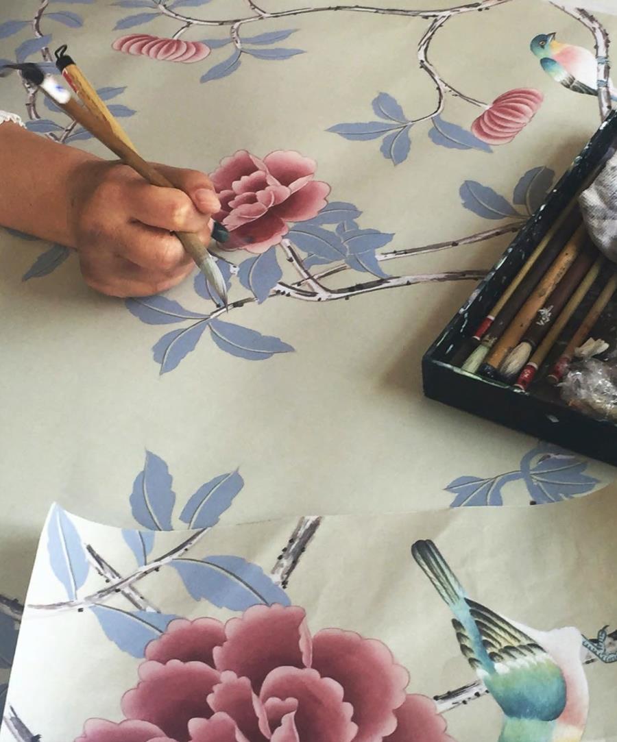 A hand painting pink flowers and blue leaves on pale silk