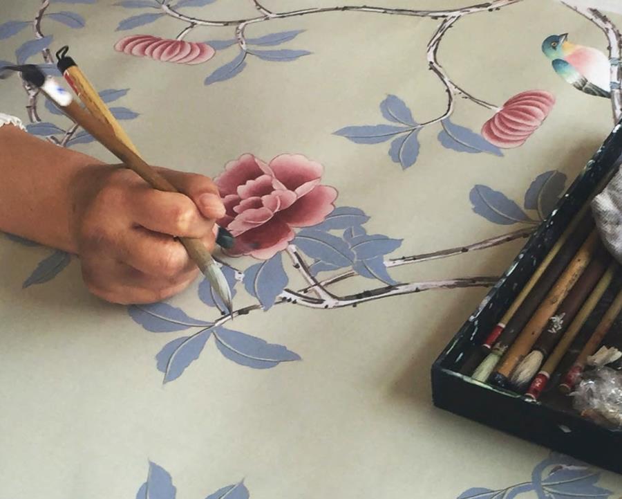A hand painting pink flowers on a pale silk ground