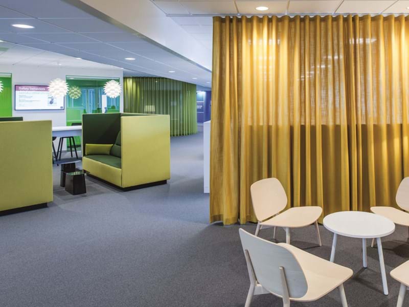 An open office with mustard curtains and green booths
