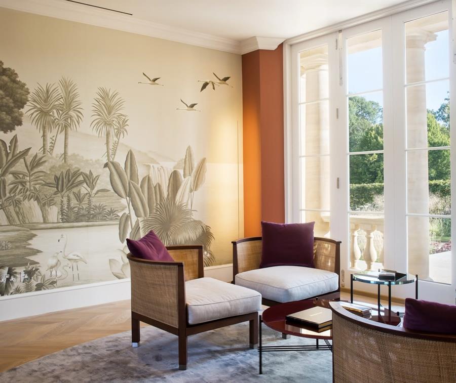 Living room with a scenic mural of palms and birds, armchairs and tall windows