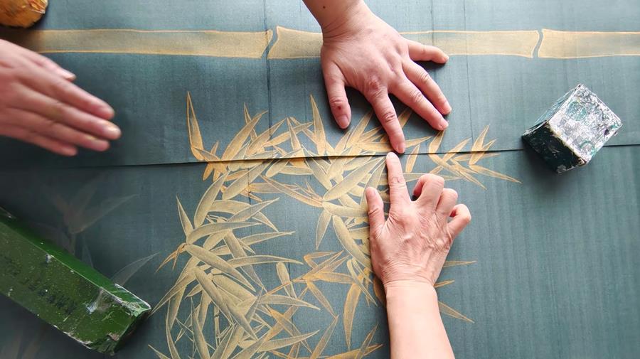 Hands tracing a gold design onto teal silk