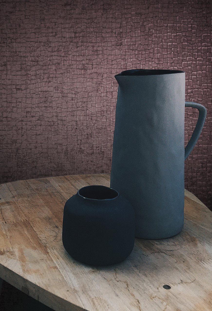 A dark textured wallcovering behind a black jug and vase