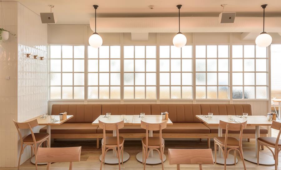 A restaurant with tan leather banquettes beneath tall windows