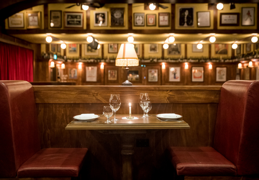 A dark restaurant with red leather booths beneath framed portraits
