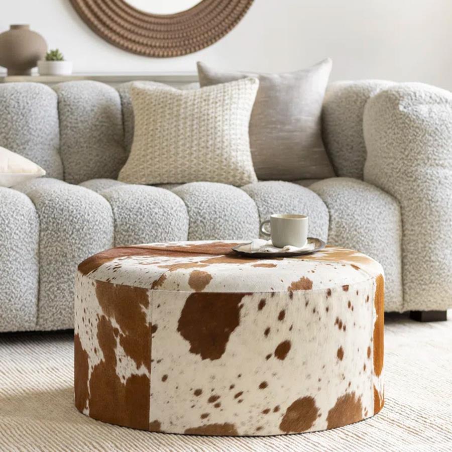A round cowhide ottoman in front of a sofa