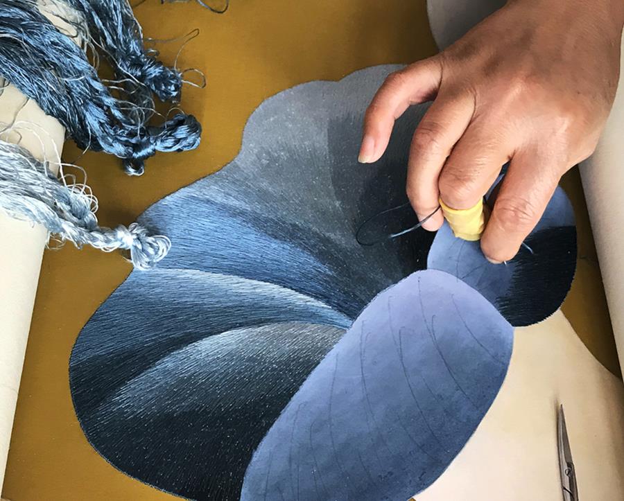 A hand working on large blue painted petals