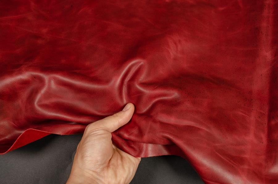 A hand pressing red waxed leather, lightening the colour