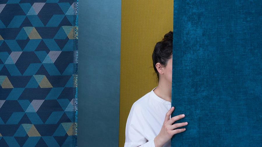 A person looking out from behind a length of blue Designtex fabric