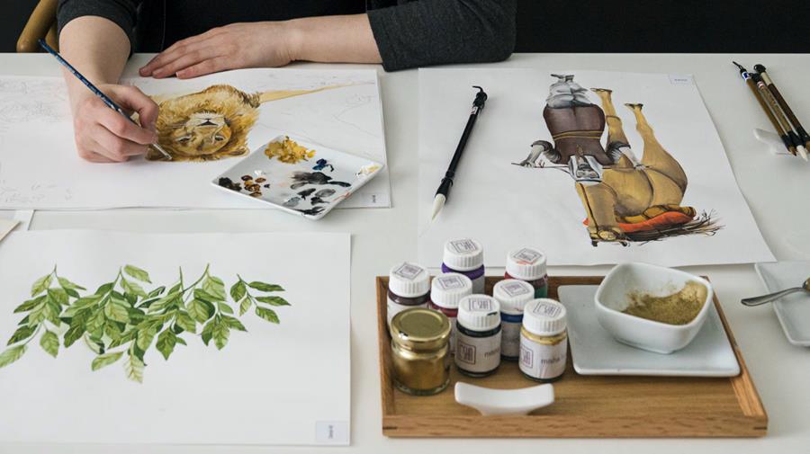 An artist painting leaves at a desk set with paint pots