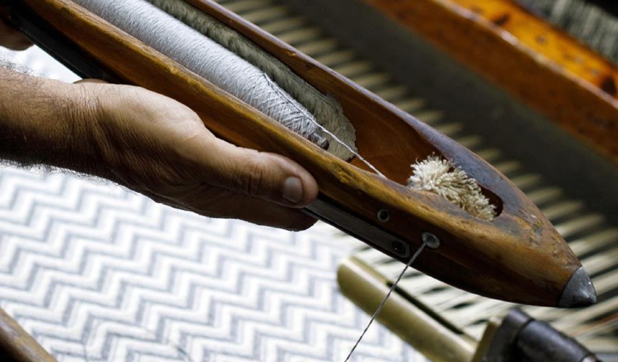 Hands working a natural woven wallcovering on a loom