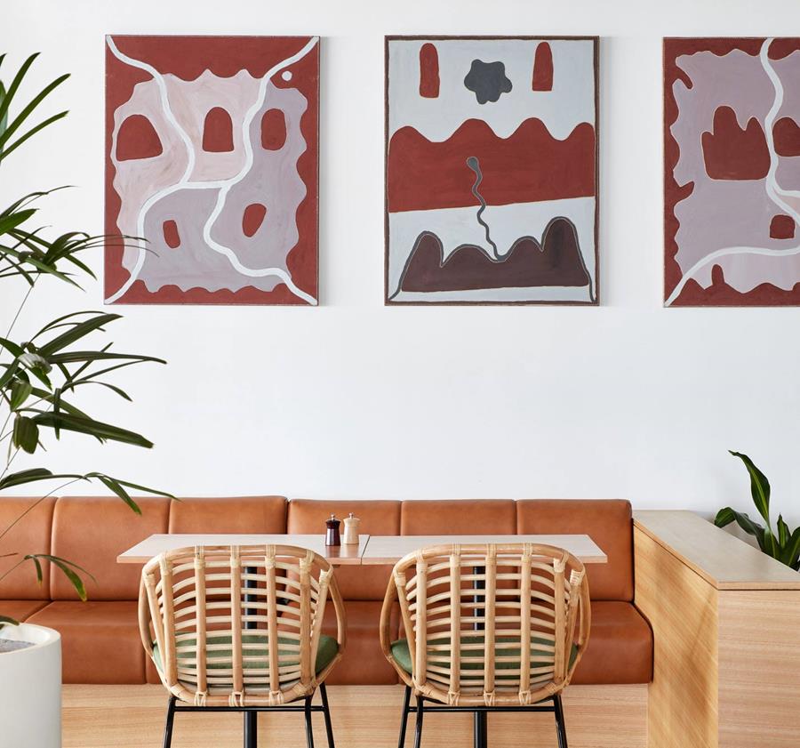 A lounge with a tan leather sofa beneath patterned artworks