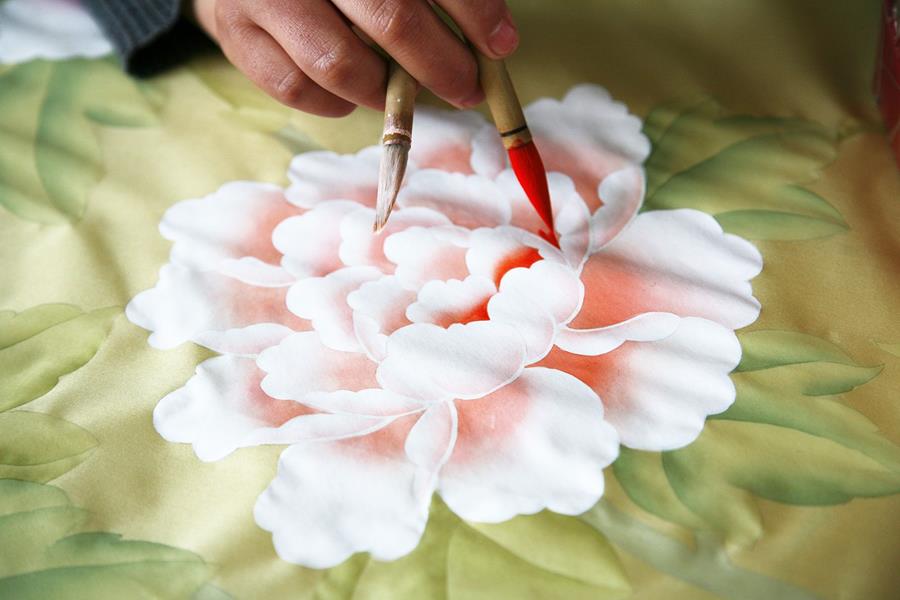 A fine brush painting a pink peony on pale green silk