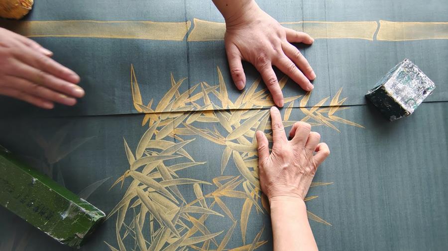 Hands tracing a gold design onto teal silk