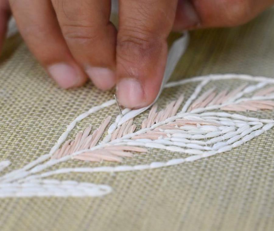Hands embroidering a feather design onto raffia