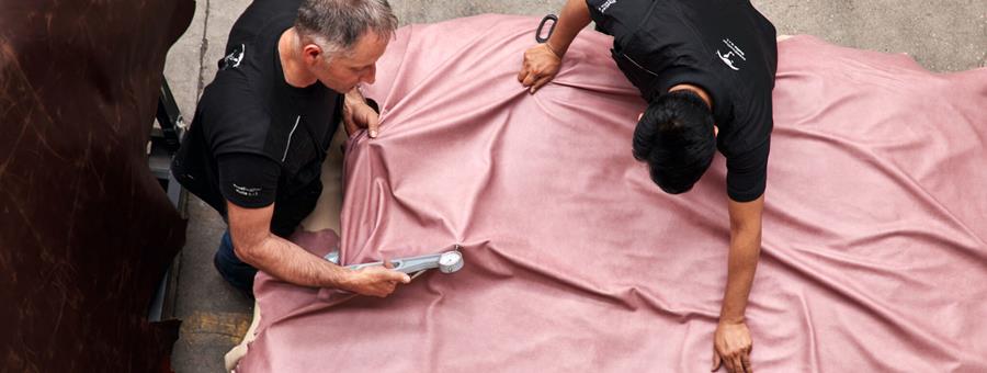 Two leather workers cutting pink leather on a table