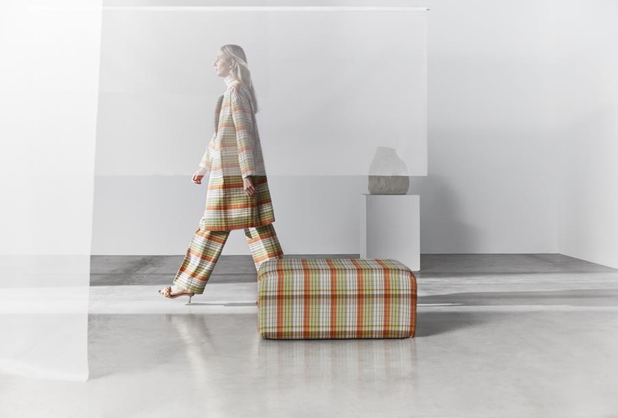 A woman walking past a Club check pouf in a pale room