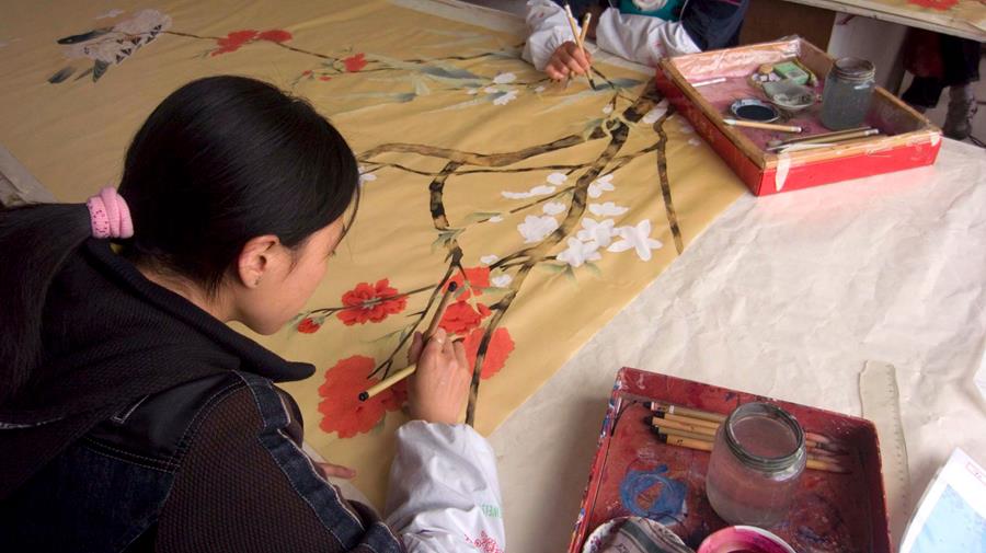 Artisans painting a long silk panel at a work table