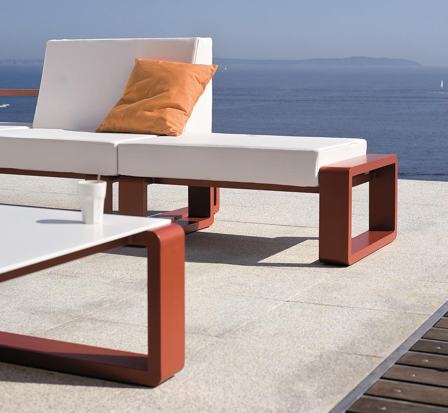 White outdoor lounge with an orange cushion on a terrace above the sea