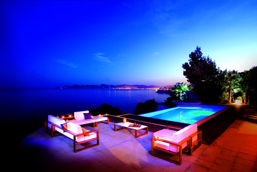 Outdoor lounge furniture beside a pool at dusk, overlooking the sea