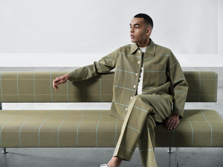 A man seated on a long bench upholstered in olive Svensson Club check