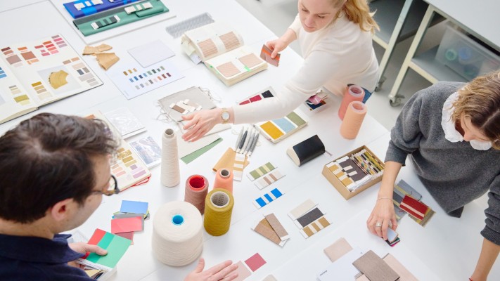 Designers at a table of colour cards, yarn cones and fabric samples