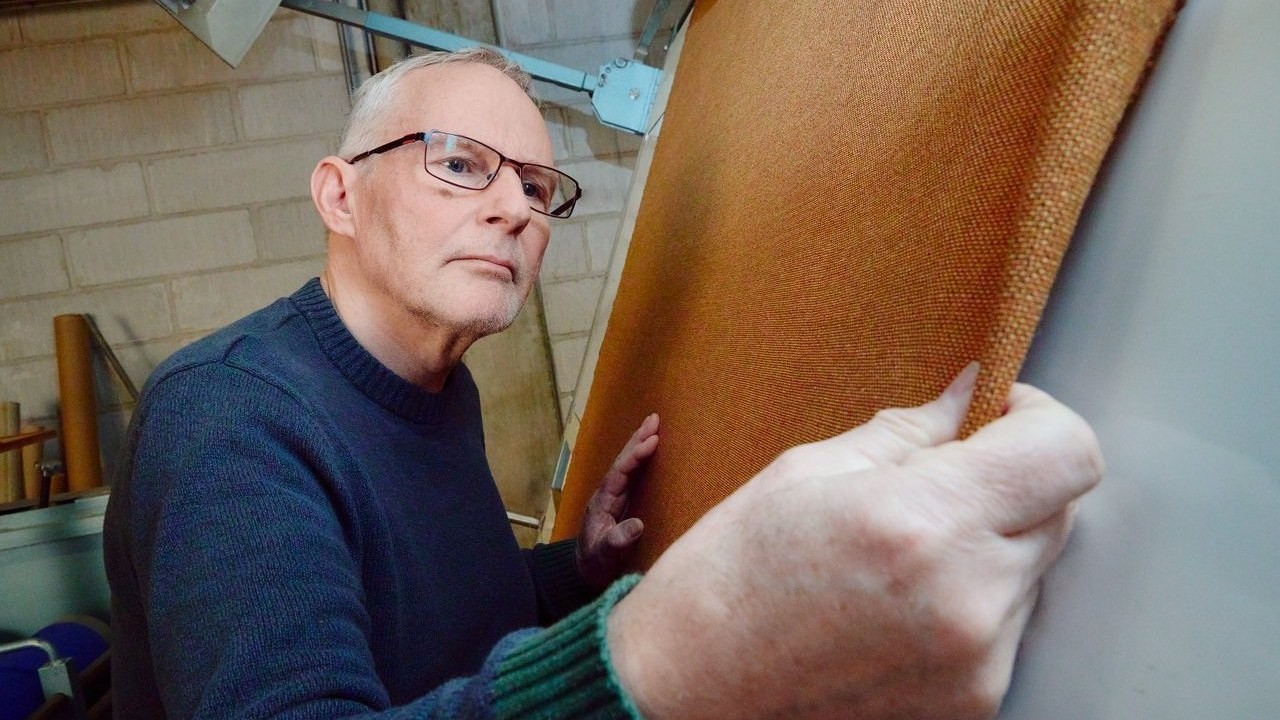 A man in glasses running his hand over ochre cloth