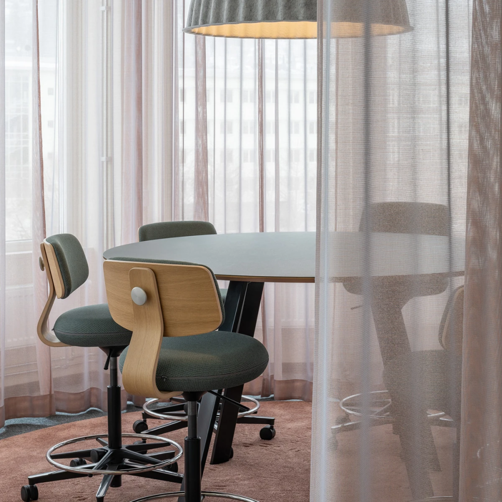 Sheer curtains drawn around a meeting table with drafting stools under a pendant light