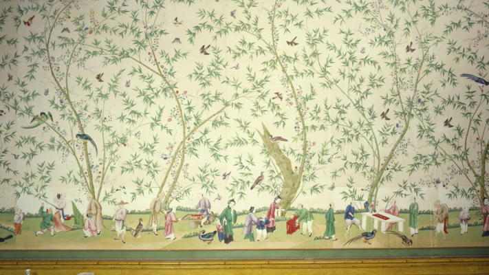 A hand-painted Chinese wallpaper: flowering trees and birds on a pale ground, with small figures along its foot