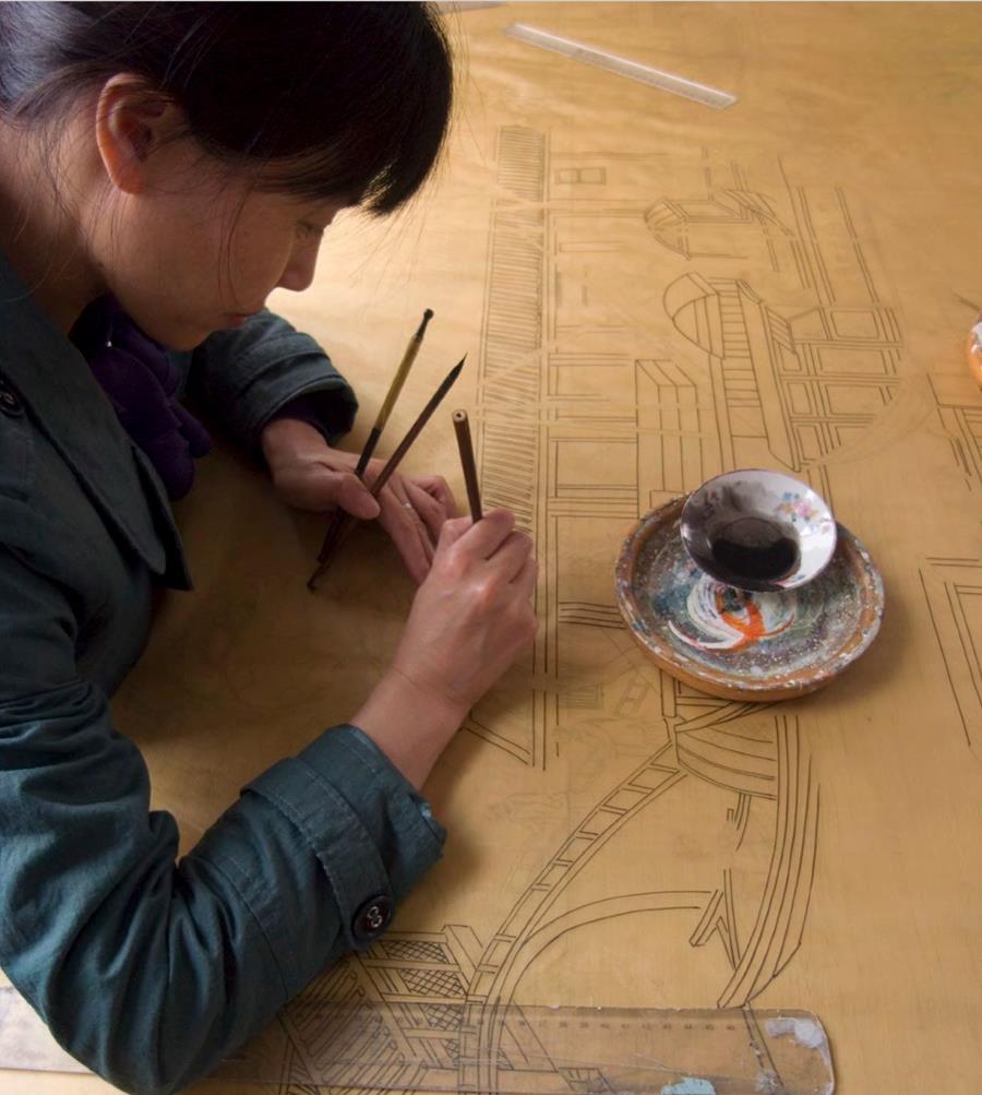 An artisan drawing fine lines on a gold ground beside a dish of paint