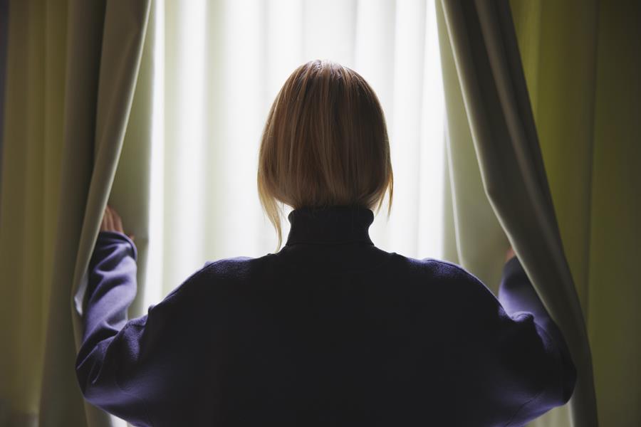 Woman drawing back dark green Svensson Tune curtains at a window